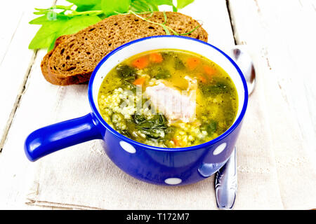 Schweinerippchen Suppe mit Couscous und Spinat in eine blaue Schüssel auf Küchenpapier, Brot auf Holzbrett Hintergrund Stockfoto