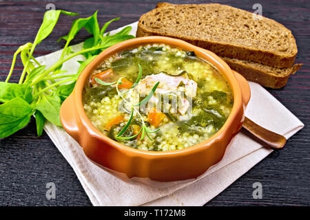 Schweinerippchen Suppe mit Couscous und Spinat in einer Schüssel auf Serviette, Brot auf dunklen Holzplatte Hintergrund Stockfoto