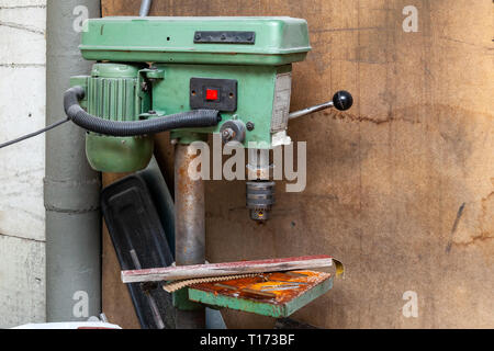 Alten vertikalen grünen Bohrmaschine mit einem großen roten Netzschalter und Rost auf dem Bügeleisen Elemente in einer industriellen Produktion Werkstatt. Werkzeug für Metall pro Stockfoto