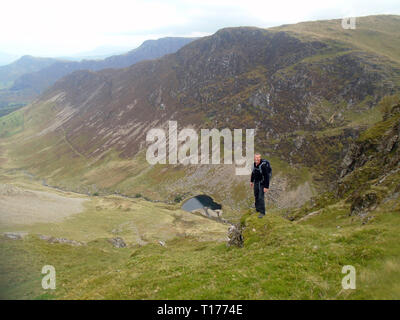 Mann stand auf Felsvorsprung über dem Behälter für Scope Beck auf dem Weg zum Wainwright Robinson, Nationalpark Lake District, Cumbria, UK. Stockfoto