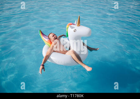Glückliche junge Mann sitzt in Weiß Schwimmer und genießen. Er lächelt und hält die Augen geschlossen. Kerl ist in Pool alleine. Stockfoto
