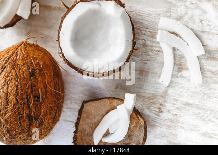 Ganze Kokosnuss und in Stücke schneiden und Chips auf einem hellen weißen Holz- Hintergrund. Stockfoto