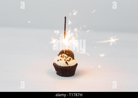 Essen, Party und Urlaub Konzept - Geburtstag Cupcake mit Wunderkerzen auf weißem Hintergrund Stockfoto