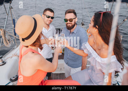 Zwei junge Frauen sitzen und Männer schauen. Alle von Ihnen halten Heem Gläser. Sie schauen sich an und lächeln. Menschen Beifall. Stockfoto