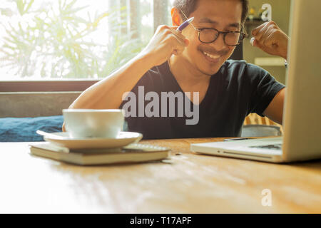 Asiatischer Mann mit Laptop erhobenen Händen bis Erfolg feiern in grosse Nachrichten Stockfoto