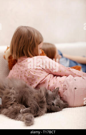 Zwei Mädchen (7 und 8 Jahre alt) gerade ein E-Buch und ein Smartphone zu Hause auf dem Sofa mit ihrer Katze. Selektive konzentrieren. Stockfoto