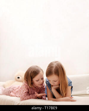 Zwei Mädchen (7 und 8 Jahre alt) gerade ein E-Buch und ein Smartphone zu Hause auf dem Sofa mit ihrer Katze. Selektive konzentrieren. Stockfoto