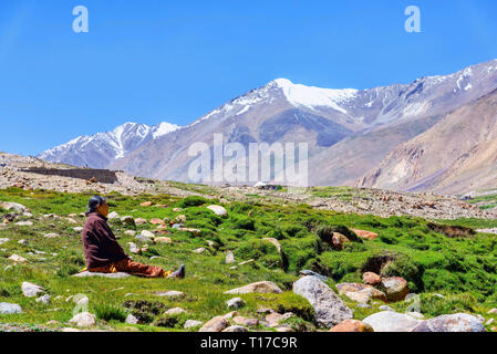 Khardung, Indien - 19. August 2015: Eine lokale Frau dunkles auf dem Gras die majestätische Bergkette vor ihr bewundern. Stockfoto