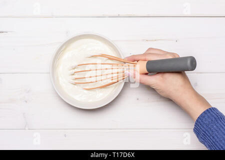 Frau Hand mischen Cottage und eine saure Sahne. Rezept Schritt für Schritt keine Backen Käsekuchen flatlay auf weißem Holz Stockfoto