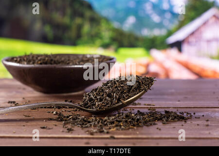 Viele Stücke von trockenen schwarzer Tee Earl Grey in einem grauen Keramik Schüssel mit silbernen Löffel mit Sommer Alpen im Hintergrund Stockfoto