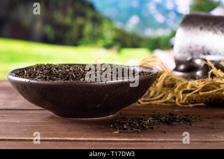 Viele Stücke von trockenen schwarzer Tee Earl Grey in einem grauen Keramik Schüssel auf Jute Tuch mit schwarzen Keramik Tasse mit Sommer Alpen im Hintergrund Stockfoto