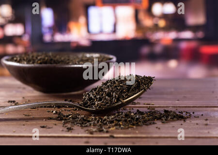 Viele Stücke von trockenen schwarzer Tee Earl Grey in einem grauen Keramik Schüssel mit silbernen Löffel mit Restaurant im Hintergrund Stockfoto