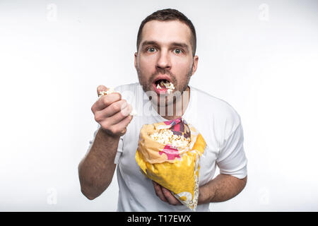 Erstaunt Kerl ist mit einer kleinen Packung mit guten Popcorn und eting. Er hat sich den Mund öffnete. Er ist nicht essen Popcorn sehr genau. Auf weiß Isoliert Stockfoto
