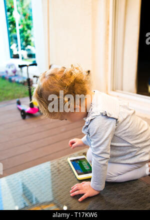 Kind lernen zum ersten Mal, wie man ein Smartphone für Unterhaltung, halten ein gelangweiltes Kind zu Hause beschäftigt. Stockfoto