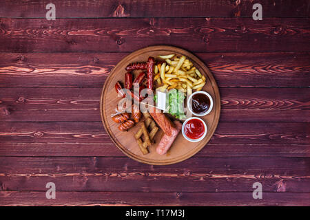 Wurst für Bier. Würstchen, Pommes frites, Cracker, Ketchup und Sauce auf dem Schneidbrett und Holz- Hintergrund. Stockfoto