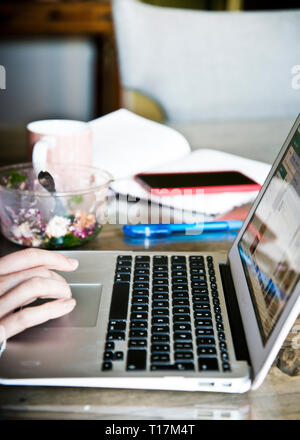 Selektives Bild von Notebook mit unordentlicher Schreibtisch zu Hause, halb gefressene Lebensmittel in Plastikbehälter, Kaffeetasse und Handy auf Notizblock gelegt, Stockfoto