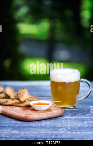 Bier Snacks. Chicken Wings auf Stöcke und Becher Bier. Auf dem Schneidbrett und grüner Sommer Hintergrund Stockfoto