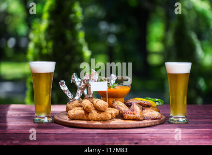Huhn und Käse für Bier und zwei Gläser Bier. Chicken Wings, käsestange und Käse Kugeln mit hellen Gemüse Sauce. Auf der Schneiden Stockfoto