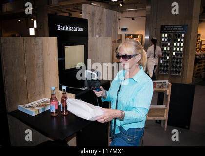 Frau mittleren Alters, die neue Technologie, Selbstscan für Shopping und Touchscreen-Technologie in einem Indoor-Stil Marktplatz umarmt.Gent, Belgien, Europa. Stockfoto