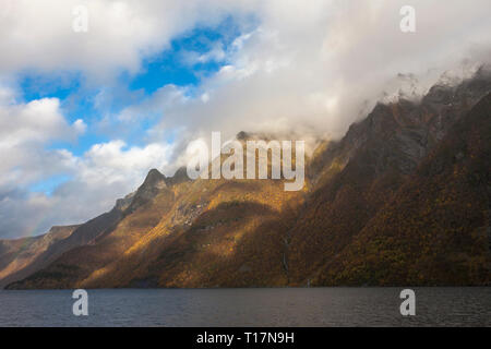 Ein Patch von Sonnenlicht beleuchtet die Berge über Hjørundfjord, Møre og Romsdal, Norwegen Stockfoto