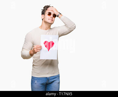 Jungen gutaussehenden Mann holding Karte mit roten Herzen über isolierte Hintergrund mit Hand betonte am Kopf, mit Scham und Überraschung Gesicht schockiert, wütend und fr Stockfoto