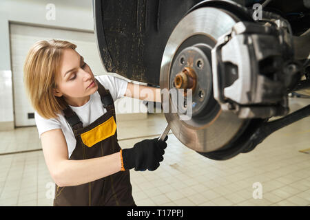 Hübsche, hübsche Mädchen in Uniform tragen, schwarze Handschuhe, Schlüssel, Spezialwerkzeug für die Instandsetzung des Fahrzeugs. Junge Mechanikerin zur Festsetzung der Bremsscheibe, Arbeiten mit Automobilen. Stockfoto