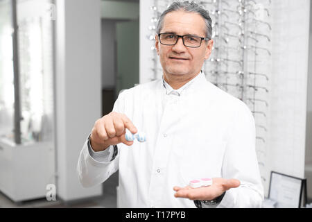 Augenarzt holding Container für Objektive und Kamera. Reifen Arzt, Augenarzt in weißen Mantel und Gläser stehen, in medizinischen Zimmer in der Klinik. Stockfoto