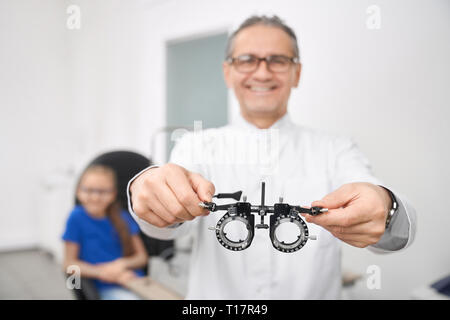 In der Nähe von Auge Test Gläser. Arzt Augenarzt in Weiß medizinische Fell spezielle Ophthalmologische Geräte für die Prüfung und die Wahl der Linsen. Patient sitzt auf Hintergrund. Stockfoto