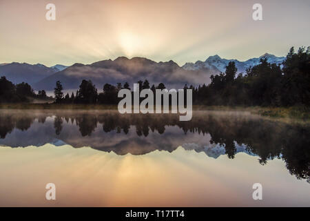 Steigende Nebel bei Sunrise schafft eine tolle Atmosphäre am Lake Matheson mit Blick auf den Mount Cook und Mount Tasman. Stockfoto