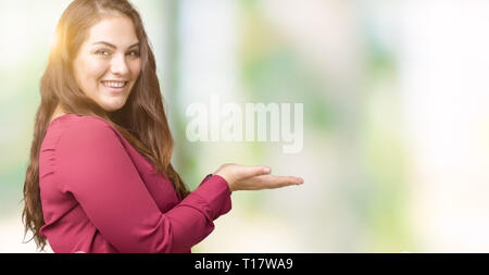 Schöne Übergrößen junge Frau über isolierte Hintergrund verweist auf die Seite mit der Hand und öffnen Sie Palm, präsentiert ad lächelte glücklich und zuversichtlich Stockfoto