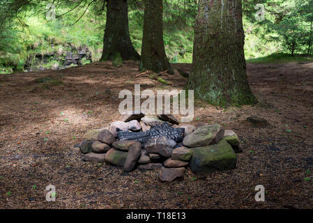 Verlassene Lager Feuer mit schwarzer Asche von Felsen umgeben. Im Wald neben Snake Pass, Derbyshire, England. Stockfoto