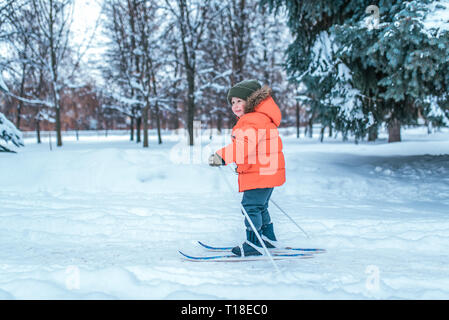 Einen kleinen Jungen von 3-6 Jahren, die im Winter in der City Park, Fahrten auf Skiern für Kinder. Freier Platz für Text. Die ersten Schritte im Sport für Kinder, ein Stockfoto