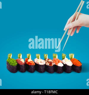 Hand mit Stäbchen wählt Sushi auf blauem Hintergrund. Stockfoto