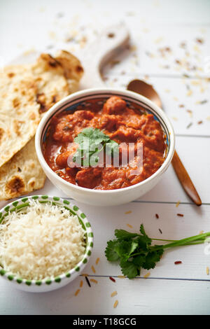 Frische und leckere Chicken Tikka Masala serviert in Keramik Schüssel. Indischen würzigen Gericht Curry. Mit Reis und Naan Brot auf den Seiten. Close Up. Flach. Stockfoto