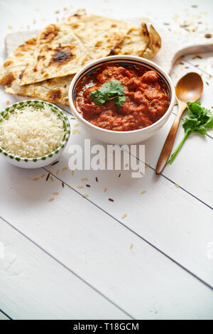 Frische und leckere Chicken Tikka Masala serviert in Keramik Schüssel. Indischen würzigen Gericht Curry. Mit Reis und Naan Brot auf den Seiten. Close Up. Flach. Stockfoto