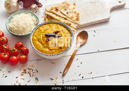 Indische beliebte Speisen Dal braten oder traditionelle Dal Tadka Curry in Keramik Schüssel mit Reis und Naan Brot serviert. Auf weissem Holztisch gelegt. Detailansicht Stockfoto