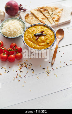 Indische beliebte Speisen Dal braten oder traditionelle Dal Tadka Curry in Keramik Schüssel mit Reis und Naan Brot serviert. Auf weissem Holztisch gelegt. Detailansicht Stockfoto