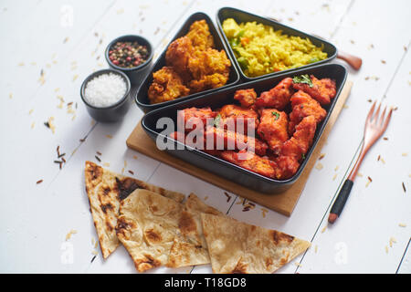 Scharfe indische gebratenes Huhn mit Curry Gemüse Reis, Zwiebel bhajia, Naan Brot serviert. Auf weissem Holztisch gelegt. Stockfoto