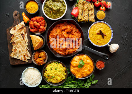 Sortiment von verschiedenen Arten der indischen Küche auf dunklen rusty Tabelle. Chicken Tikka Masala, Butter, Nilgiri, Daal Tarka. Mit gebratener Reis serviert, Naan bre Stockfoto