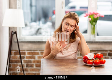 Frau, Kopfschmerzen und Hautausschlag auf der Haut nach dem Verzehr von Tomaten Stockfoto