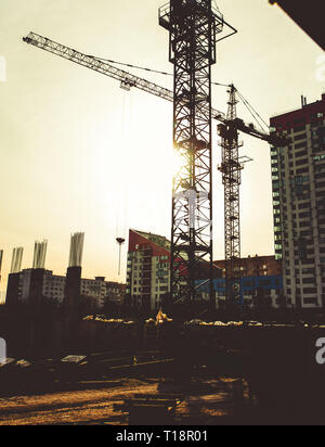 Baustelle mit Hochhäusern Block im Bau in einem städtischen Umfeld durch eine große industrielle Kran gegen Sonnenuntergang Himmel Silhouette dominiert Stockfoto