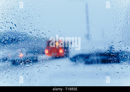 Verkehr Abstract im Winter. Verkehr von in einem Auto gesehen. Wassertropfen auf der Windschutzscheibe und Auto Rückleuchten im Bokeh Stockfoto