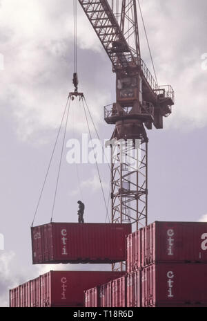 Archiv von zwei Männern, die Arbeitnehmer hoch oben auf der Luft Shipping Container per Kran aus Stack & gesenkt im Depot London England Großbritannien zu Boden angehoben wird Stockfoto