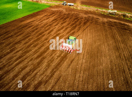 Ein Landwirt auf einem roten Traktor mit einer Sämaschine Sauen Korn in gepflügten Land in einem privaten Feld im Bereich Village. Stockfoto