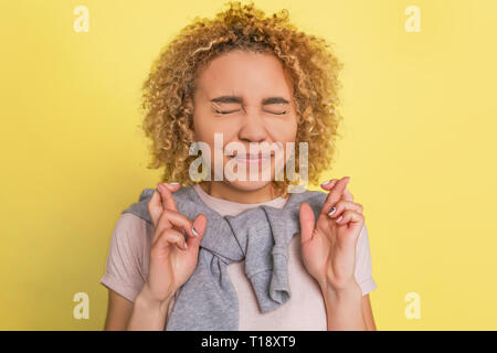 Ein gril kreuzt ihre Finger. Sie hält die Augen geschlossen. Auf gelbem Hintergrund Stockfoto