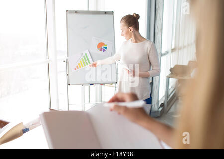 Business woman erklärt Bedeutung der verschiedenen Diagramme auf dem Flipchart. Mädchen mit dem Notebook ist das Hören von ihr und bereit, unten einige t zu schreiben Stockfoto