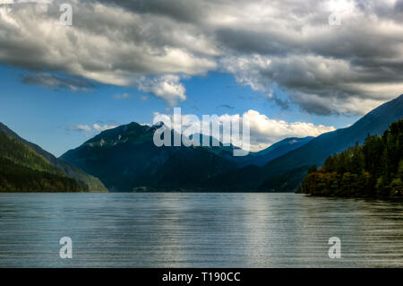 Mit Blick über den Lake Crescent mit dunklen tiefen blauen Berge in der Ferne und flauschigen weissen Wolken und blauer Himmel Stockfoto