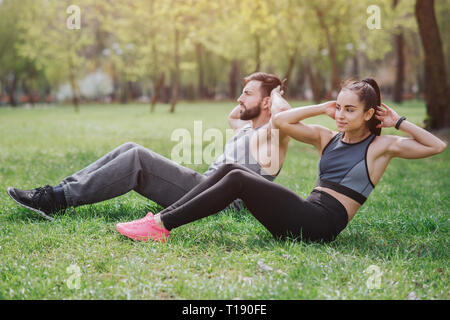 Starke und leistungsfähige Menschen Arbeiten draußen im Park. Sie tun abs-Übungen. Junger Mann und Frau suchen ernsthafte und cocnentrated Stockfoto