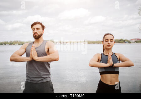 Ruhige und friedliche Bild der junge Mann und die Frau zu meditieren. Sie halten ihre Hände zusammen und stehen mit geschlossenen Augen. Sie sind stehen Stockfoto