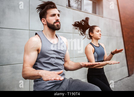 Bärtiger Kerl auf dem Platz ohne sich vorwärts zu bewegen und berühren die Hände mit den Knien. Er tut das mit seinem Partner - schlankes Mädchen. Sie sind Stockfoto